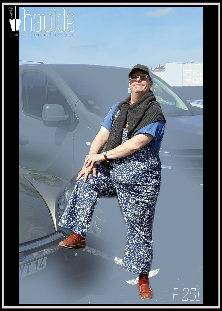 homme debout pied posé sur le parechoc d'un véhicule vêtu d'une salopette bleue imprimée papillons blancs