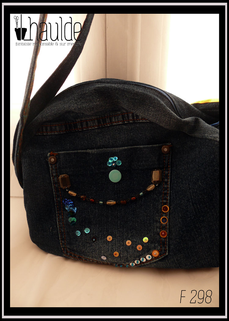 sac en forme de lapin en jean sombre, détail de la poche extérieure droite, poche arrière de jeans avec une pression bleu pâle et des sequins brodés. Une chainette de perles de verre court d'un bout à l'autre de la poche