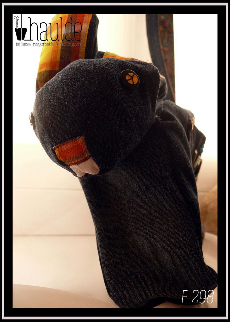 sac en forme de lapin en jean sombre, vu de face, détail de la tête avec les yeux en gros sequin dorés à paillettes, intérieur des oreilles et truffe en madras jaune, dents mimées par du tissu blanc plié.