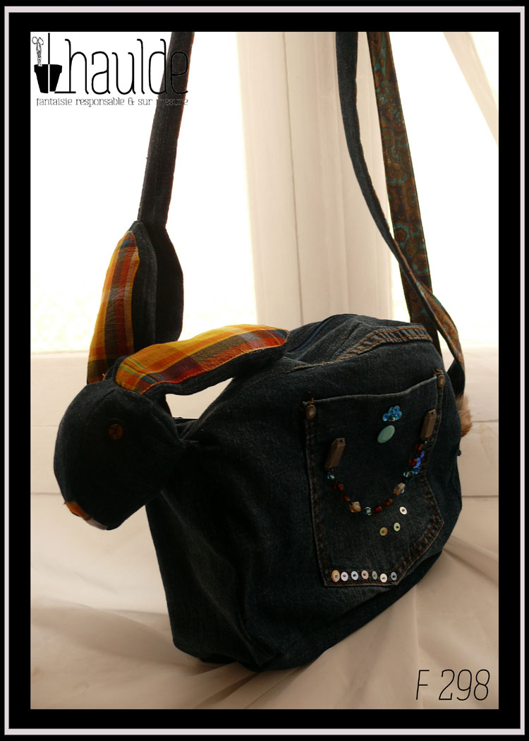 sac en jean sombre en forme de lapin, intérieur des oreilles et truffes en madras jaune, doublure intérieure en coton imprimé motifs végétaux de type paisley jaune-orangé sur fond bleu Vu suspendu par la bandoulière, de profil