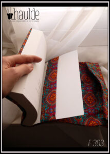 Protège livre en coton imprimé motifs psychédéliques sur fond bleu vert, dominante orange. Elastique rouge Vue de la bride entourant le dos du livre