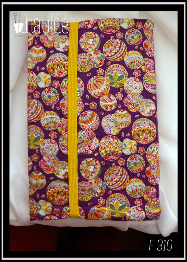 Protège livre en tissu violet imprimé temari (balles brodées japonaises) multicolores Vu fermé par son élastique jaune