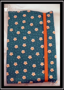 Protège-livre en coton vert foncé imprimé petites fleurs orange pâle et points blancs, vu fermé par un élastique orange