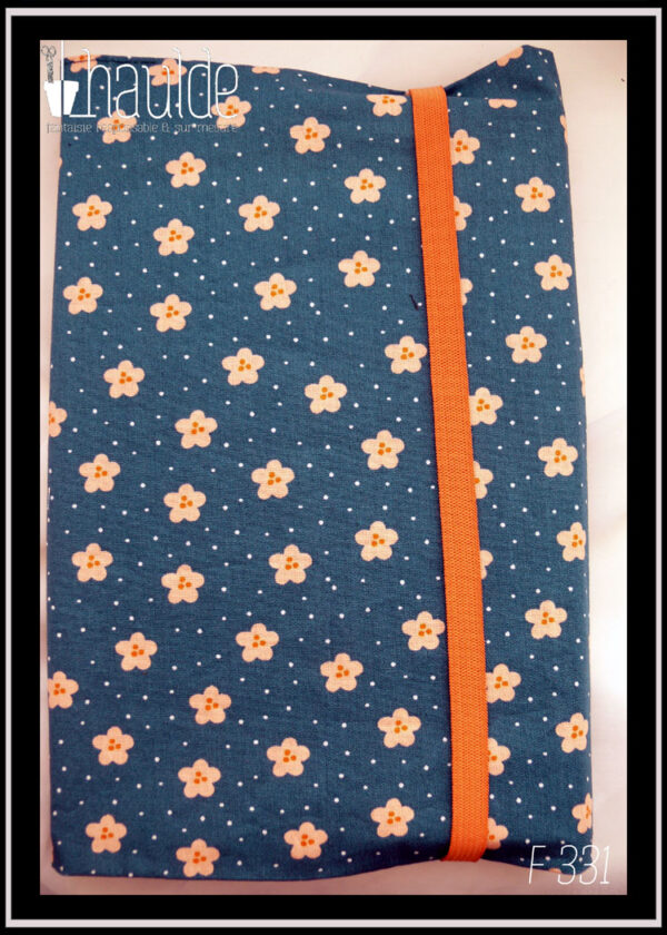 Protège-livre en coton vert foncé imprimé petites fleurs orange pâle et points blancs, vu fermé par un élastique orange