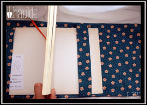 Protège-livre en coton vert foncé imprimé petites fleurs orange pâle et points blancs, vu ouvert, intérieur dans le même tissu, signet orange