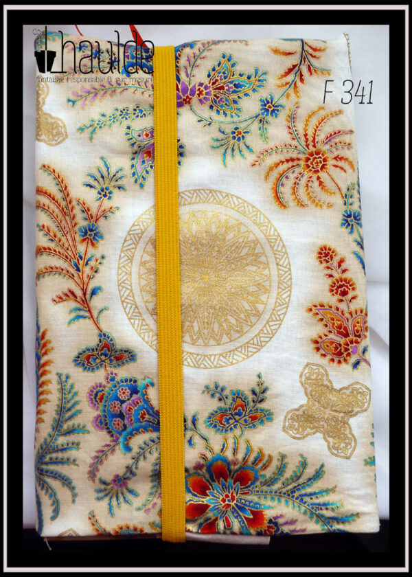 Protège livre en tissu écru imprimé motifs végétaux et floraux d'esthétique asiatique multicolores et bordés de doré. Vu fermé par un élastique jaune