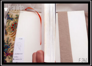 Protège livre en tissu écru imprimé motifs végétaux et floraux d'esthétique asiatique multicolores et bordés de doré. Vu ouvert, signet en satin orange et doublure en coton beige