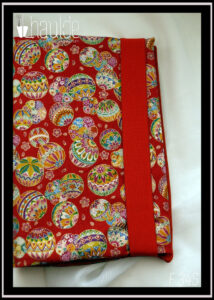 Protège livre en tissu rouge imprimé temari (balles brodées japonaises) multicolores Vu fermé par un élastique rouge large