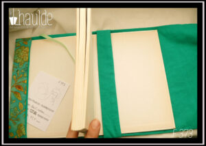 protège livre en tissu vert imprimé feuillage doré Vu ouvert avec un livre à l'intérieur, doublure en tissu vert, marque page en satin vert pâle