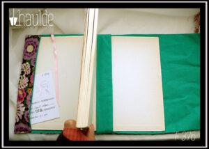 Protège livre en tissu noir imprimé grosses fleurs mauves, violettes et roses, avec du doré, vu ouvert avec un livre, intérieur vert, marque page en satin rose pâle