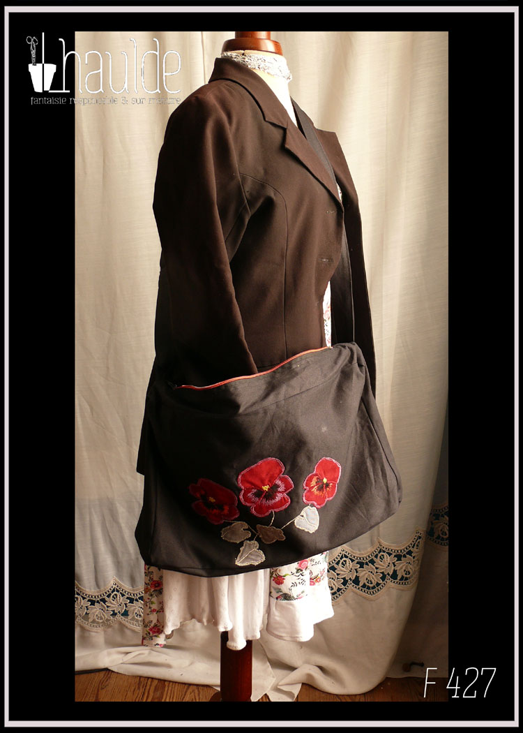 Sac en sergé noir, grand format horizontal à bandoulière, avec des appliqués en forme de pensées rouges avec leurs feuilles. Le centre des fleurs, les contours et les tiges sont brodés à la machine Vu porté sur un mannequin de couture