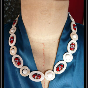 Collier constitués de perles en verre blanc opaque alterné avec des ellipses de nacre ayant au centre une perle oblongue de verre de bohème rouge à inclusion fleurie bleue, blanche et jaune, cercles de nacre avec au centre une perle blanche vu sur un mannequin de couture par dessus un chemisier en satin bleu (F 484) Le fermoir vintage est décoré d'une fausse petite perle et se pince pour s'ouvrir