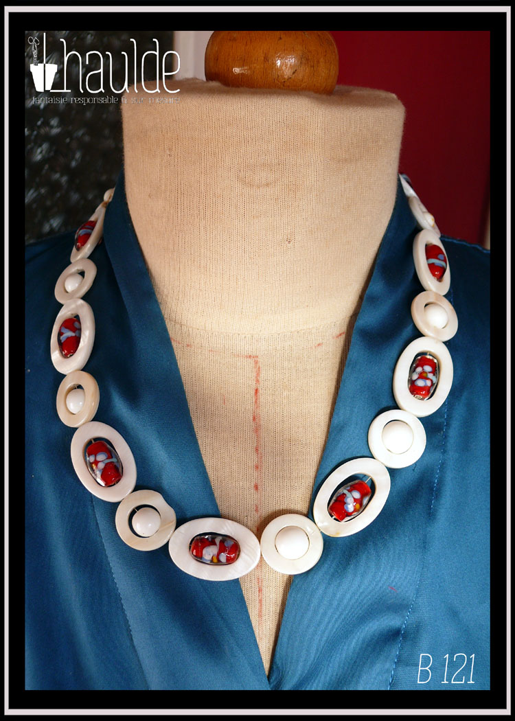 Collier constitués de perles en verre blanc opaque alterné avec des ellipses de nacre ayant au centre une perle oblongue de verre de bohème rouge à inclusion fleurie bleue, blanche et jaune, cercles de nacre avec au centre une perle blanche vu sur un mannequin de couture par dessus un chemisier en satin bleu (F 484) Le fermoir vintage est décoré d'une fausse petite perle et se pince pour s'ouvrir
