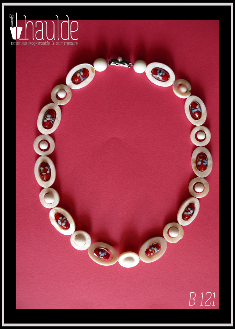 Collier constitués de perles en verre blanc opaque alterné avec des ellipses de nacre ayant au centre une perle oblongue de verre de bohème rouge à inclusion fleurie bleue, blanche et jaune, cercles de nacre avec au centre une perle blanche vu de dessus posé sur un papier rose Le fermoir vintage est décoré d'une fausse petite perle et se pince pour s'ouvrir