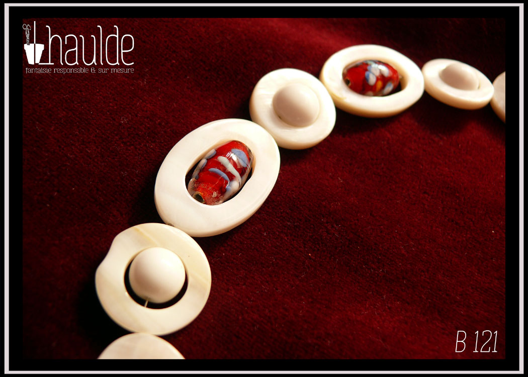 vu en gros plan de quelques cercles et ellipses de nacre et leurs perles au centre, verre de bohème oblong rouge à inclusion fleurie ou perle en verre blanc opaque