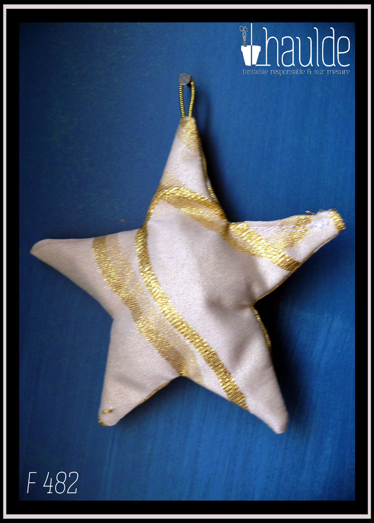 Etoile à cinq branches en tissu rembourré blanc pailletés traversé de lignes dorées Vue suspendue à un clou sur un fond bleu