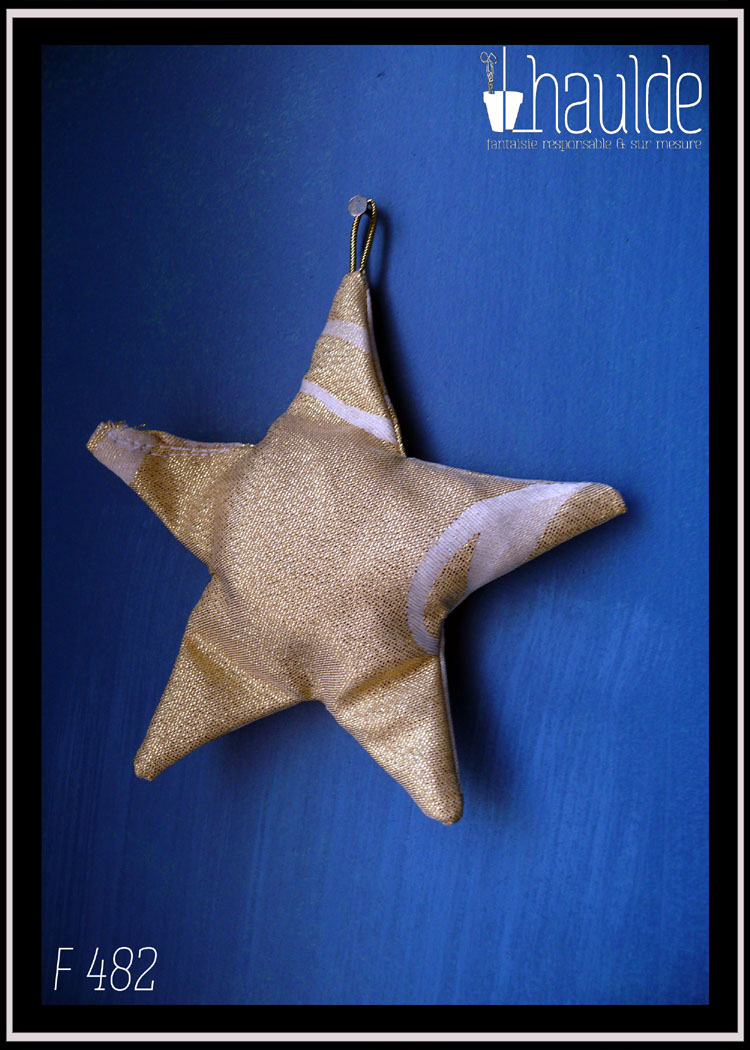 Etoile à cinq branches en tissu rembourré doré traversé de lignes blanches pailletées Vue suspendue à un clou sur un fond bleu