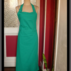 Tablier de potier vert moyen assez éclatant, vu sur un mannequin de couture dans un couloir.