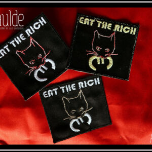 trois patchs "eat the rich" (mange les riches) presque carrés noirs, une tête de chat qui tient dans sa gueule le symbole de l'euro, le texte "eat the rich" est tout en haut du patch. La tête du chat est une simple ligne avec les yeux et la moustache, soit rose chamarré soit rose pâle, le texte et le symbole euro sont soit en blanc soit légèrement jaune (fil phosphorescent) Vu sur un morceau de tissu rouge