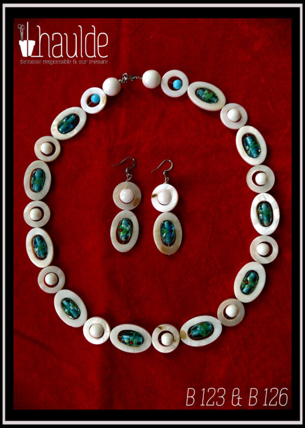 parure collier +paire de boucles d'oreilles. Le collier est constitué d'ellipses de nacre blanc alternées avec des cercles de nacre blanc, à l'intérieur de chaque ellipse il y a une perle en verre de Bohème oblongue vert pâle à incrustation fleurs turquoise et rouge. A l'intérieur de chaque cercle une perle en verre blanc opaque. Le fermoir est un mousqueton flanqué de deux grosses perles en verre blanc opaque et de cercle de nacre avec une petite perle turquoise au centre Les boucles d'oreilles sont montées sur crochet d'acier et composées d'une ellipse de nacre blanc avec en son centre une perle en verre de Bohème identique à celles du collier, surmontée d'un cercle de nacre avec en son centre une perle de jade blanc Vus posés sur du velours rouge vif