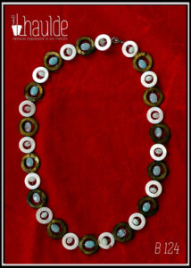Collier composé de cercles de nacre mordoré avec en leur centre une perle ovale plate en verre bleu pâle transparent, alternés avec des cercles de nacre blanc un peu plus petits avec en leur centre un petit galet de verre bleu pâle transparent Vu de dessus sur du velours rouge vif