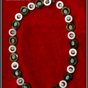 Collier composé de cercles de nacre mordoré avec en leur centre une perle ovale plate en verre bleu pâle transparent, alternés avec des cercles de nacre blanc un peu plus petits avec en leur centre un petit galet de verre bleu pâle transparent Vu de dessus sur du velours rouge vif