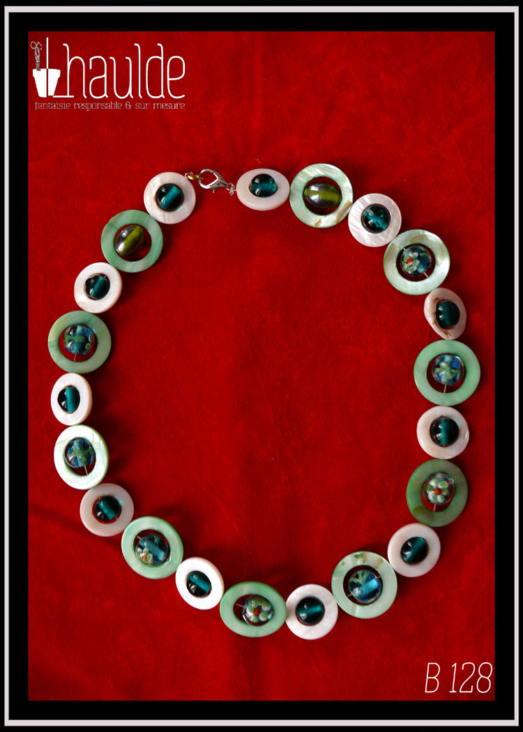Collier, fermoir à mousqueton, composé de cercles de nacre vert pâle avec en leur centre une perle ronde en verre de Bohème turquoise pâle à inclusion fleurs vert blanc et orange, alternés avec des cercles de nacre blanc plus petits avec en leur centre une perle de verre transparent bleu paon Vu de dessus sur du velours rouge vif