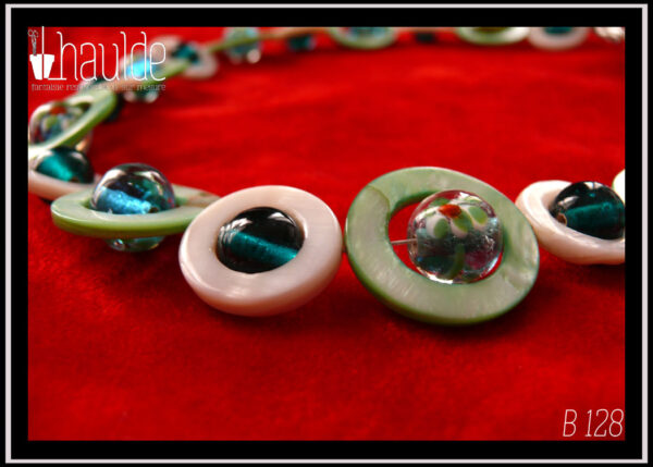 Vue en gros plan du collier, fermoir à mousqueton, composé de cercles de nacre vert pâle avec en leur centre une perle ronde en verre de Bohème turquoise pâle à inclusion fleurs vert blanc et orange, alternés avec des cercles de nacre blanc plus petits avec en leur centre une perle de verre transparent bleu paon
