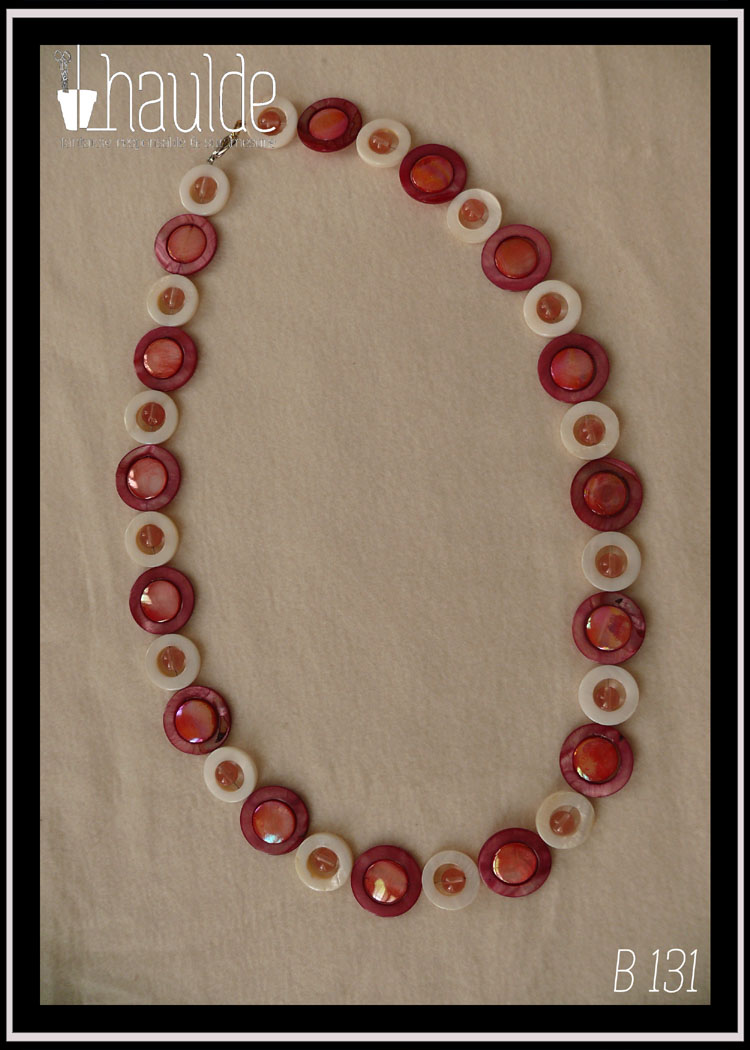 Collier composé de cercles de nacre blanc avec une perle de cristal rose en leur centre alternés avec des cercles de nacre rouges avec un palet de nacre rose irisé en leur centre Vu de dessus posé sur de la polaire blanche