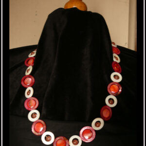 Collier composé de cercles de nacre blanc avec une perle de cristal rose en leur centre alternés avec des cercles de nacre rouges avec un palet de nacre rose irisé en leur centre Vu autour du cou d'un mannequin de couture vêtu de velours noir