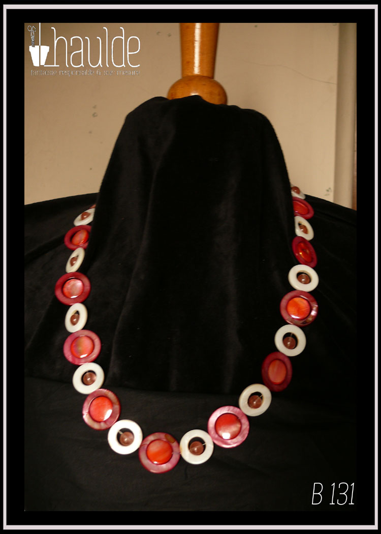 Collier composé de cercles de nacre blanc avec une perle de cristal rose en leur centre alternés avec des cercles de nacre rouges avec un palet de nacre rose irisé en leur centre Vu autour du cou d'un mannequin de couture vêtu de velours noir