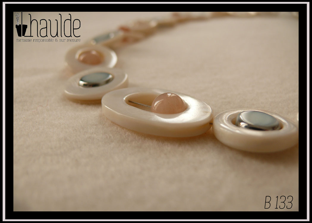 Collier composé de cercles de nacre blanc avec un palet de nacre bleu en leur centre, alterné avec des cercles de nacre blanc plus petits avec une perle d'aventurine rose pâle en leur centre. Au milieu du collier les petits cercles de nacre ont une perle en verre bleu pâle plate à tranche d'acier en leur centre et sont alternés avec des ellipses de nacre blanc avec une perle d'aventurine rose en leur centre Vue en gros plan