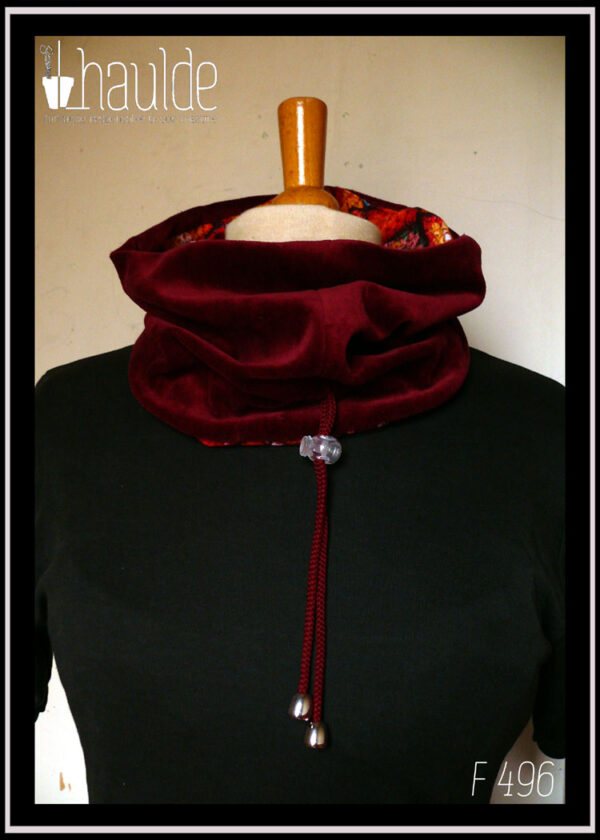 cache-col montant en jersey imprimé "granny squares", des carrés de crochets multicolores, dominante rouge. Doublure en velours rouge bordeaux, cordon rouge bordeaux avec des clochettes pour protéger les bouts et un serre-cordon transparent. Vu côté velours sur un mannequin de couture