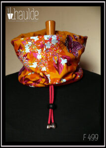 cache col en tissu jaune imprimé papillons pourpres, motifs végétaux multicolores à dominante fuchsia et orange, doublure en french terry (jersey épais) jaune ocre Cordon rose, bouts protégés par des clochettes argentées, serre-cordon noir. Vu côté tissu imprimé sur un mannequin de couture