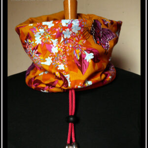 cache col en tissu jaune imprimé papillons pourpres, motifs végétaux multicolores à dominante fuchsia et orange, doublure en french terry (jersey épais) jaune ocre Cordon rose, bouts protégés par des clochettes argentées, serre-cordon noir. Vu côté tissu imprimé sur un mannequin de couture