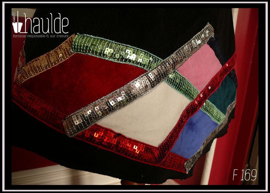 Vue de détail du bas de la mini jupe trapèze en velours milleraies noir, losanges de velours rouge, rose pâle, blanc, bleu roi et bleu pétrole encadré de galons de sequins doré, vert, argent, rouge et rouge-rose