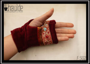 Mitaine en velours rouge bordeaux, garnie de deux galons brodés, un large brodé de losanges dorés avec au centre un cercle soit rouge bordeaux, soit bleu pâle, soit rose pâle et garni de petits sequins circulaires dorés, le deuxième plus étroit en satin rouge bordeaux brodé de motifs géométriques (pointes de flèche) dorés et verts foncés Les galons sont placés entre les phalanges et le milieu de l'ouverture pour le pouce Vue portée côté paume