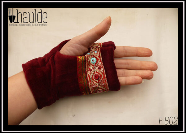 Mitaine en velours rouge bordeaux, garnie de deux galons brodés, un large brodé de losanges dorés avec au centre un cercle soit rouge bordeaux, soit bleu pâle, soit rose pâle et garni de petits sequins circulaires dorés, le deuxième plus étroit en satin rouge bordeaux brodé de motifs géométriques (pointes de flèche) dorés et verts foncés Les galons sont placés entre les phalanges et le milieu de l'ouverture pour le pouce Vue portée côté paume
