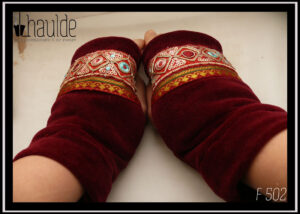 Mitaine en velours rouge bordeaux, garnie de deux galons brodés, un large brodé de losanges dorés avec au centre un cercle soit rouge bordeaux, soit bleu pâle, soit rose pâle et garni de petits sequins circulaires dorés, le deuxième plus étroit en satin rouge bordeaux brodé de motifs géométriques (pointes de flèche) dorés et verts foncés Les galons sont placés entre les phalanges et le milieu de l'ouverture pour le pouce Vue de dessus de la paire portée