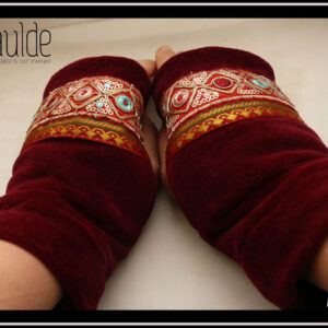 Mitaine en velours rouge bordeaux, garnie de deux galons brodés, un large brodé de losanges dorés avec au centre un cercle soit rouge bordeaux, soit bleu pâle, soit rose pâle et garni de petits sequins circulaires dorés, le deuxième plus étroit en satin rouge bordeaux brodé de motifs géométriques (pointes de flèche) dorés et verts foncés Les galons sont placés entre les phalanges et le milieu de l'ouverture pour le pouce Vue de dessus de la paire portée