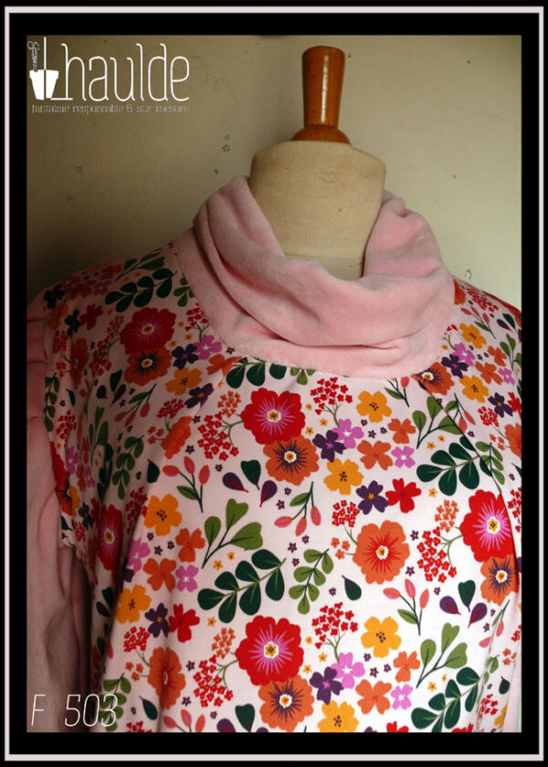 Tunique manches longues à col drapé Devant et dos en jersey rose pâle imprimé fleuri à dominante rouge orangé grappe de feuilles type acacia vertes et petites fleurs mauves et violettes éparses Manches et col en velours rose pâle Vue de détail du haut de la tunique, le jersey est plié de chaque côté du col