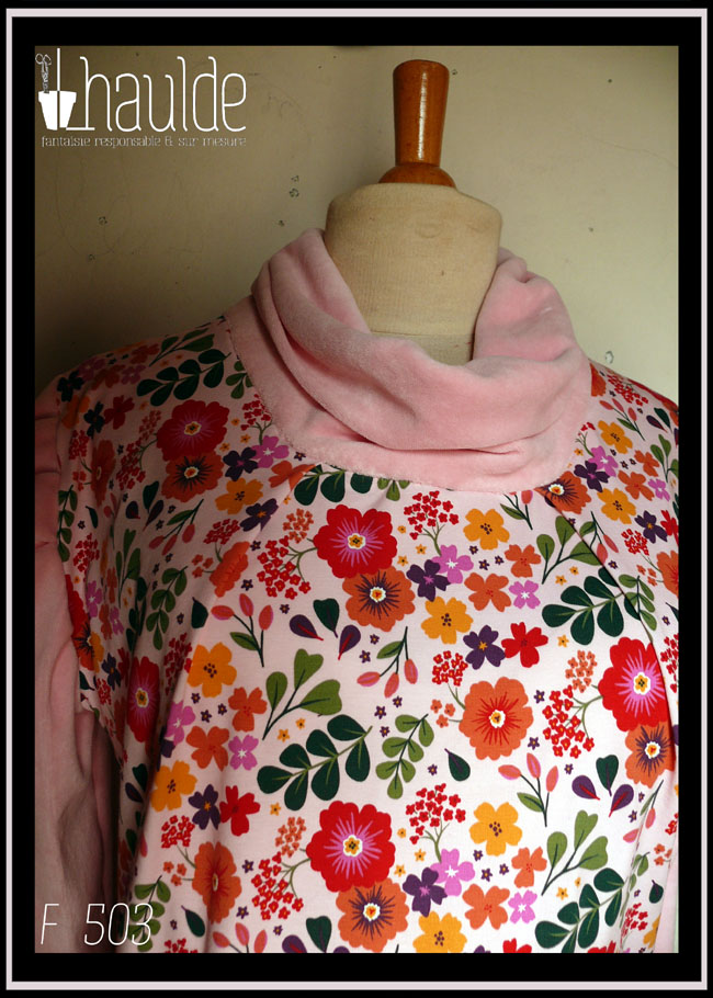 Tunique manches longues à col drapé Devant et dos en jersey rose pâle imprimé fleuri à dominante rouge orangé grappe de feuilles type acacia vertes et petites fleurs mauves et violettes éparses Manches et col en velours rose pâle Vue de détail du haut de la tunique, le jersey est plié de chaque côté du col