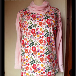 Tunique manches longues à col drapé Devant et dos en jersey rose pâle imprimé fleuri à dominante rouge orangé grappe de feuilles type acacia vertes et petites fleurs mauves et violettes éparses Manches et col en velours rose pâle Vue de face sur un mannequin de couture