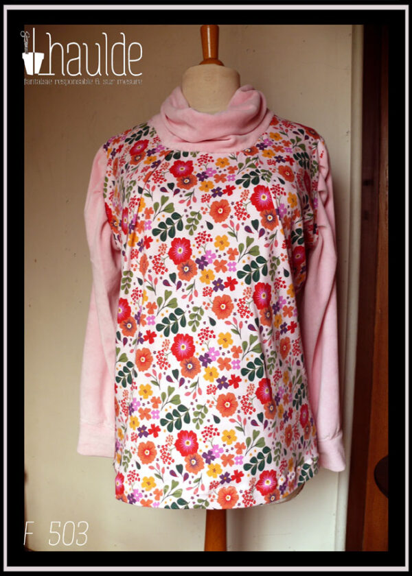 Tunique manches longues à col drapé Devant et dos en jersey rose pâle imprimé fleuri à dominante rouge orangé grappe de feuilles type acacia vertes et petites fleurs mauves et violettes éparses Manches et col en velours rose pâle Vue de face sur un mannequin de couture