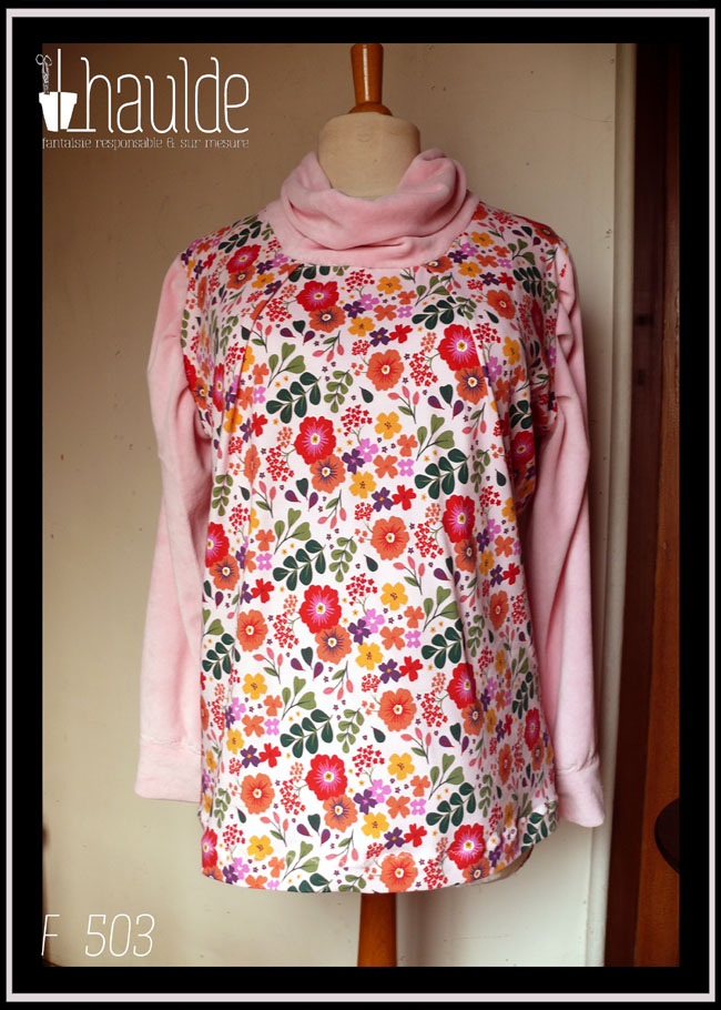 Tunique manches longues à col drapé Devant et dos en jersey rose pâle imprimé fleuri à dominante rouge orangé grappe de feuilles type acacia vertes et petites fleurs mauves et violettes éparses Manches et col en velours rose pâle Vue de face sur un mannequin de couture