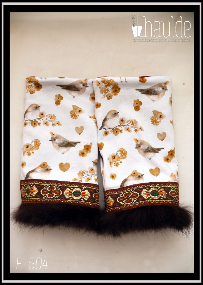 paire de mitaines vue posées sur un fond blanc Jersey blanc imprimé petits oiseaux et petites fleurs dans les tons gris, rosés et ocres Elles sont garnies à une extrémité d'un galon marron brodé de motifs abstraits vaguement floraux dorés oranges et verts avec des la fourrure marron