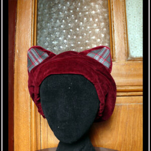 Bonnet à oreilles de chat en velours rouge bordeaux, intérieur des oreilles en écossais gris, bordeaux et rose. Vu porté par une tête de mannequin