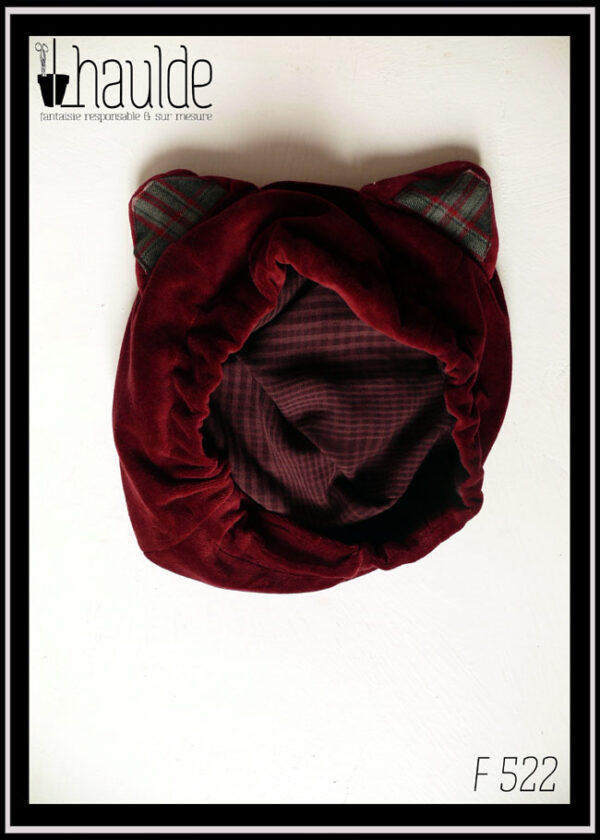 Bonnet à oreilles de chat en velours rouge bordeaux, intérieur des oreilles en écossais gris, bordeaux et rose. La doublure est en tencel à petits carreaux violets sur fond mauve que l'on voit ici puisque le bonnet est posé sur une surface blanche