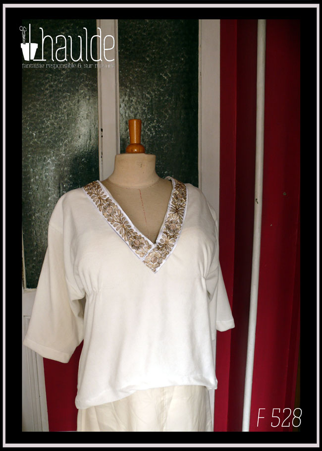 Haut manches kimono trois quarts en velours blanc écru, encolure en V profonde soulignée par un galon brodé de motifs floraux et végétaux dorés. Vu de face sur un mannequin de couture