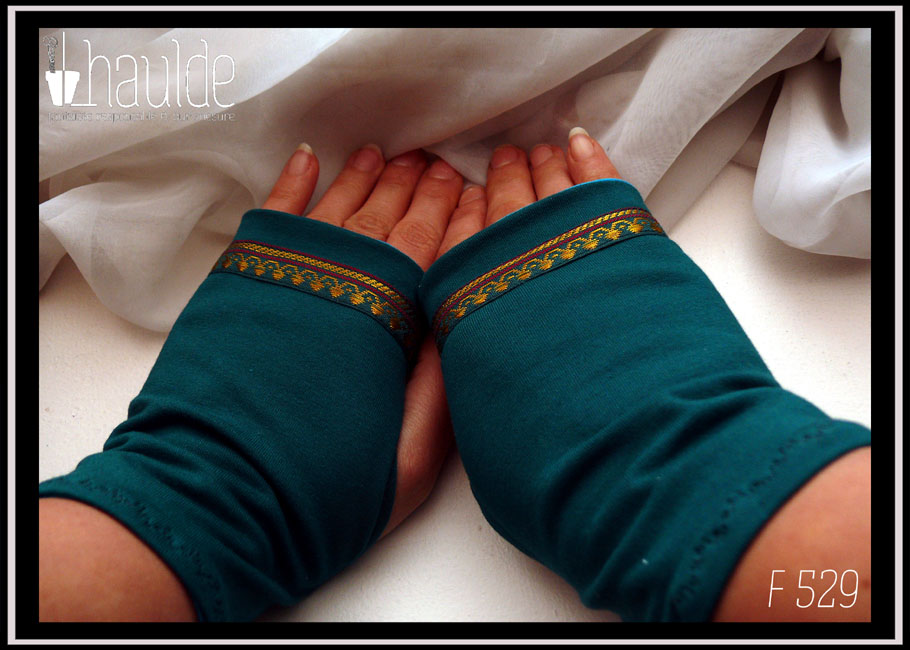 Mitaines en jersey bleu pétrole avec un galon au niveau des phalanges Il fait environ 15mm de large, fond bleu paon foncé, motifs dorés abstraits qui évoquent des pointes de flèches et deux lignes pourpres Vue de la paire, vue de dessus, portée